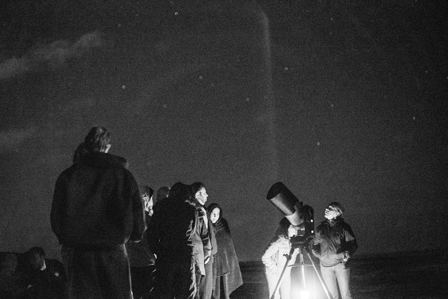 Dark night sky with several people near a telescope